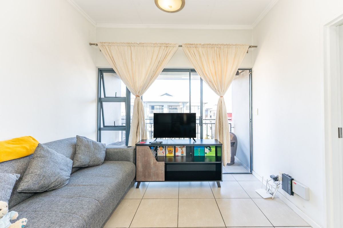 A compact living room featuring neutral tiled flooring and a large sliding glass door that provides access to an outdoor balcony area.