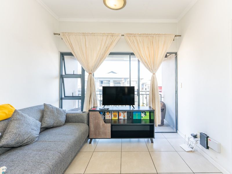 A compact living room featuring neutral tiled flooring and a large sliding glass door that provides access to an outdoor balcony area.