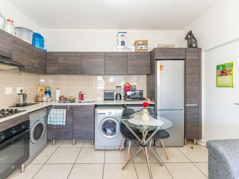 A functional kitchen featuring dark wood-look cabinetry, tiled splashbacks, integrated appliances, and tiled flooring, providing a practical and efficient workspace.