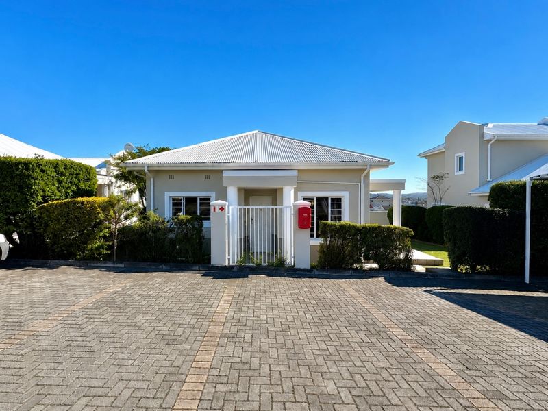 Front elevation of a townhouse featuring a paved driveway, secure gated entrance, and a well-maintained facade with a pitched roof.