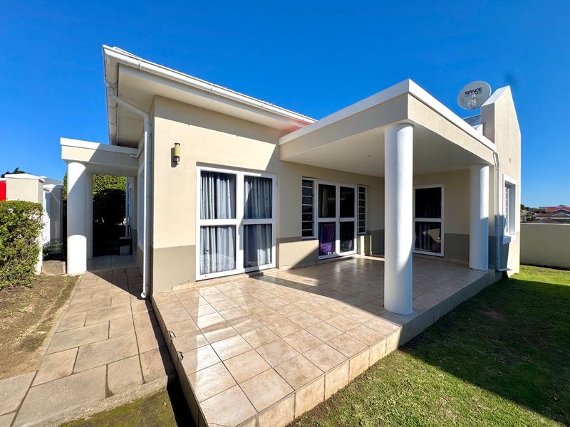 A spacious covered patio featuring tiled flooring and structural columns, providing direct access to the interior through multiple sliding glass doors.