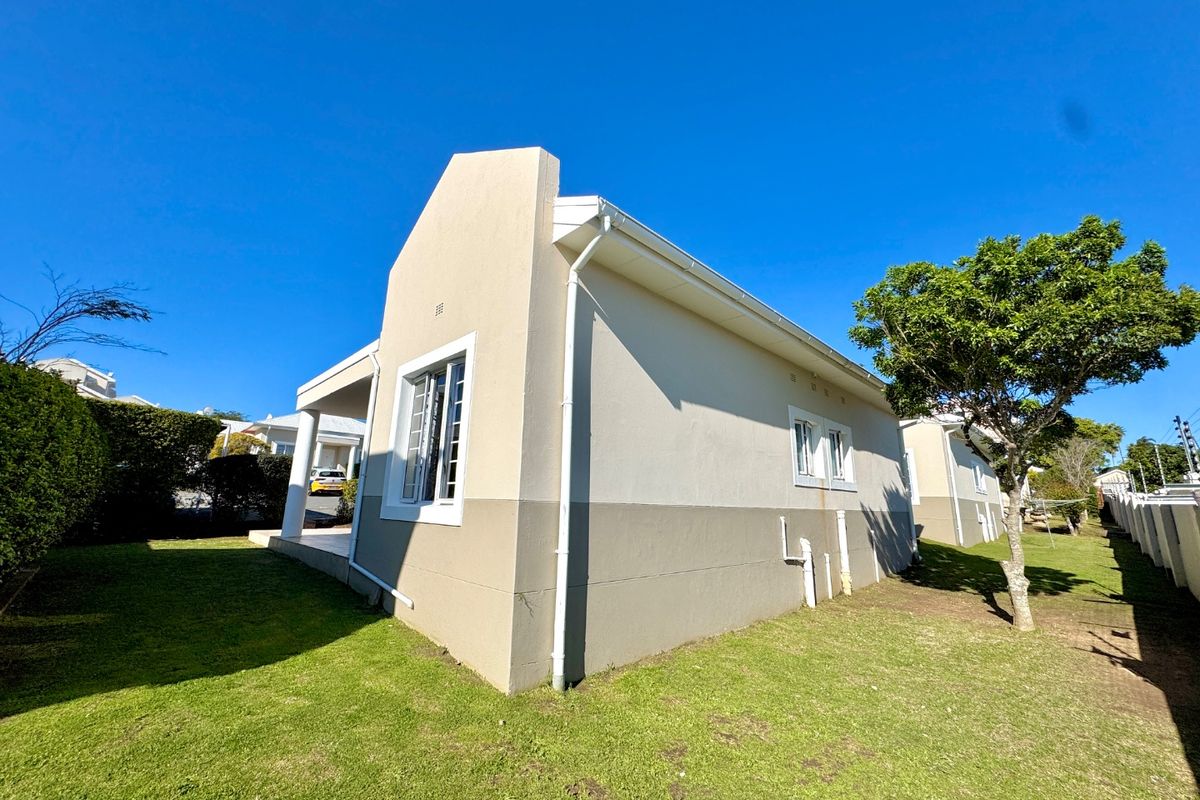 Rear exterior view of the townhouse featuring a covered patio, landscaped garden area, and visible external plumbing fixtures.