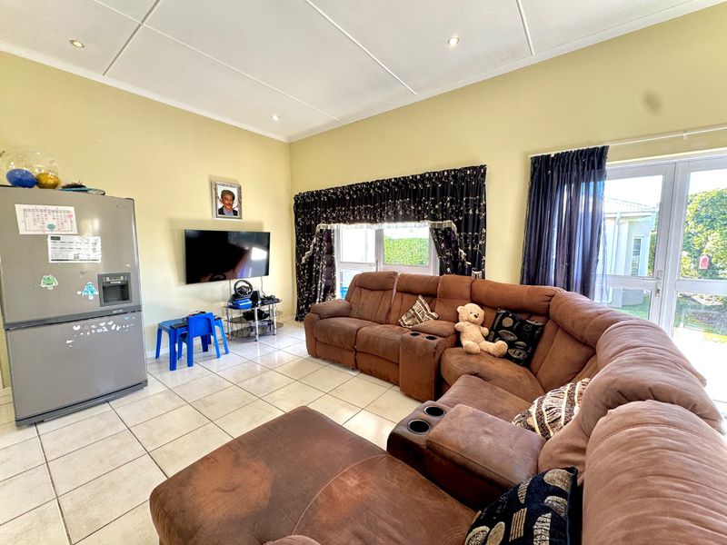 A spacious living room featuring tiled flooring, recessed ceiling lighting, and direct access to the garden through double glass doors.