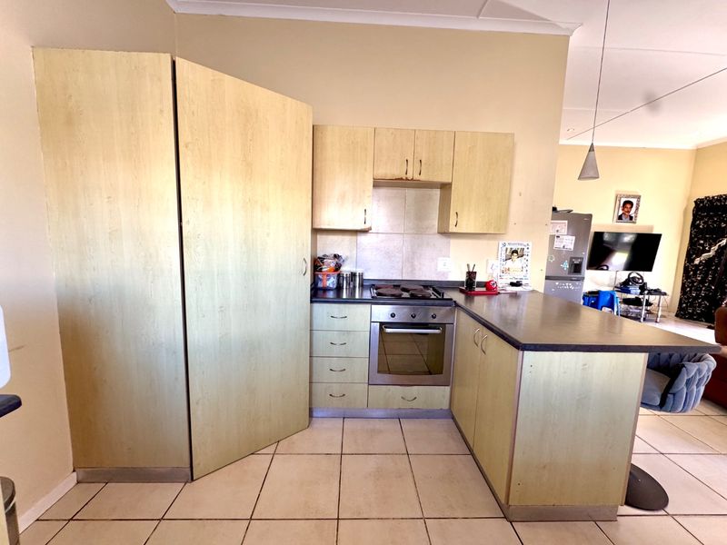 Functional kitchen featuring light-toned cabinetry, integrated oven and hob, dark laminate countertops, and tiled flooring, offering a practical layout for daily meal preparation.