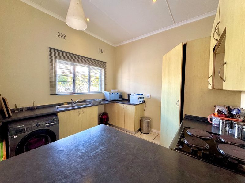 Functional kitchen featuring laminate cabinetry, dark countertops, double basin sink, and built-in electric hob, offering a practical layout with ample storage space.