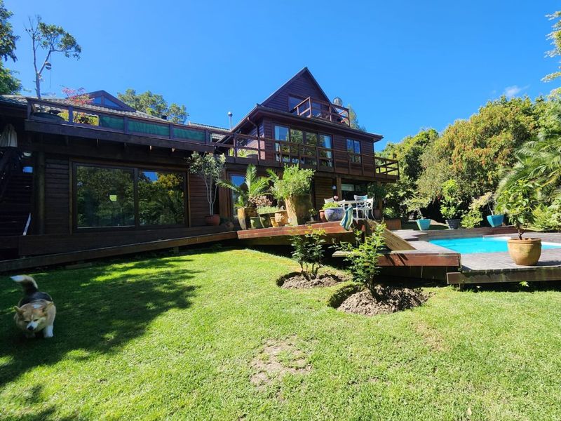 Rear view of a multi-level timber-clad house featuring extensive decking, a swimming pool, and a well-maintained garden area.