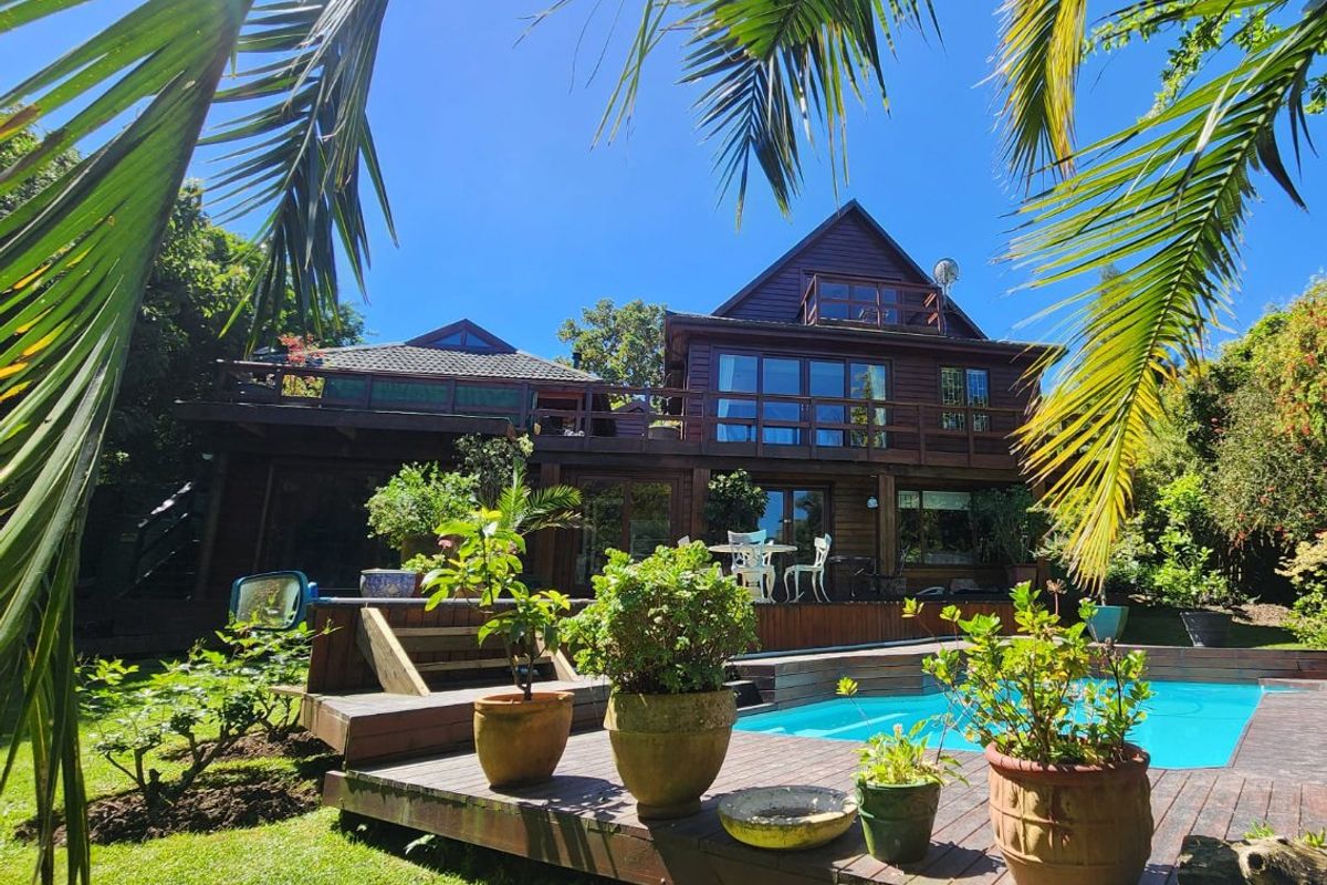 Rear view of a multi-story timber-clad house featuring a swimming pool, expansive wooden decking, and a balcony overlooking the garden.