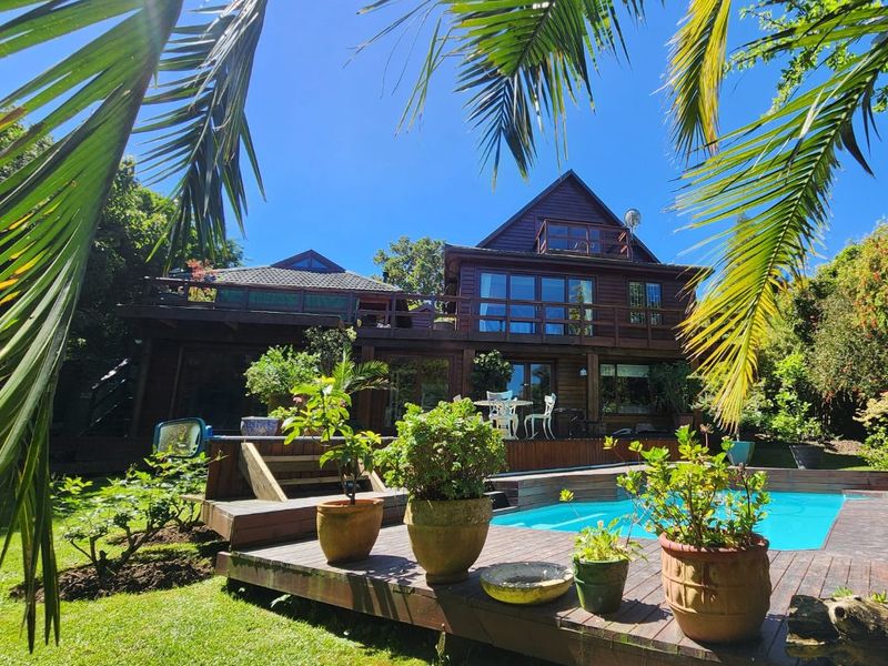 Rear view of a multi-story timber-clad house featuring a swimming pool, expansive wooden decking, and a balcony overlooking the garden.