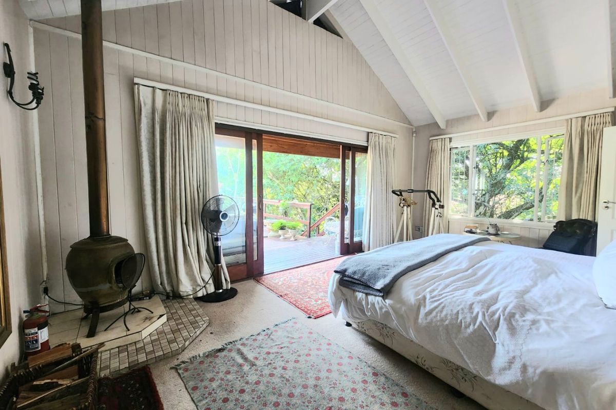 Spacious bedroom featuring a vaulted ceiling with exposed beams, a cozy wood-burning fireplace, and large sliding doors opening onto a private timber deck.