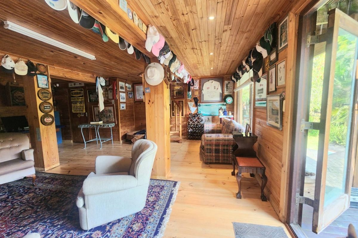 A rustic living room featuring extensive timber wall and ceiling cladding, timber flooring, and large sliding glass doors providing access to the outdoors.