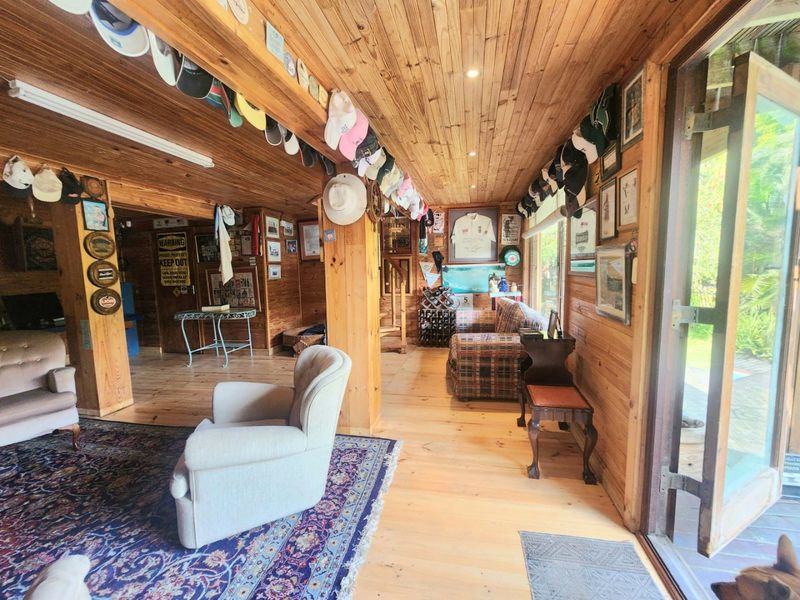 A rustic living room featuring extensive timber wall and ceiling cladding, timber flooring, and large sliding glass doors providing access to the outdoors.