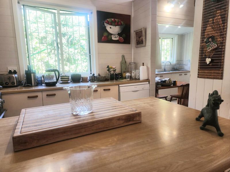 Open plan kitchen area featuring timber cabinetry, laminate countertops, and a central island, with a view through to an adjacent scullery or prep space.