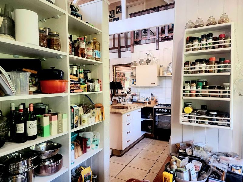 A functional scullery and pantry area featuring extensive built-in shelving, tiled flooring, and a view through to the main kitchen area.