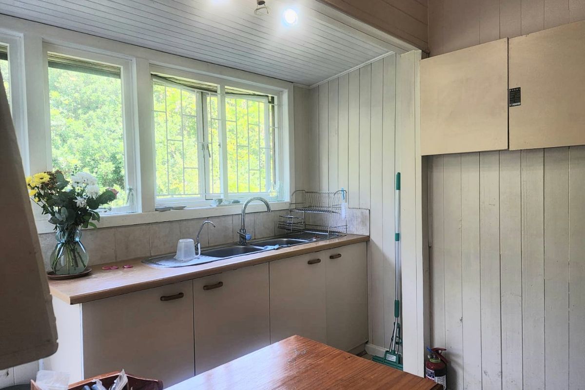A functional kitchen area featuring timber cabinetry, a double sink with mixer tap, and timber wall paneling, offering potential for a modern renovation.