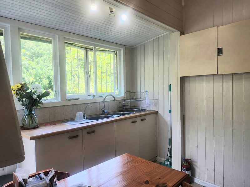A functional kitchen area featuring timber cabinetry, a double sink with mixer tap, and timber wall paneling, offering potential for a modern renovation.