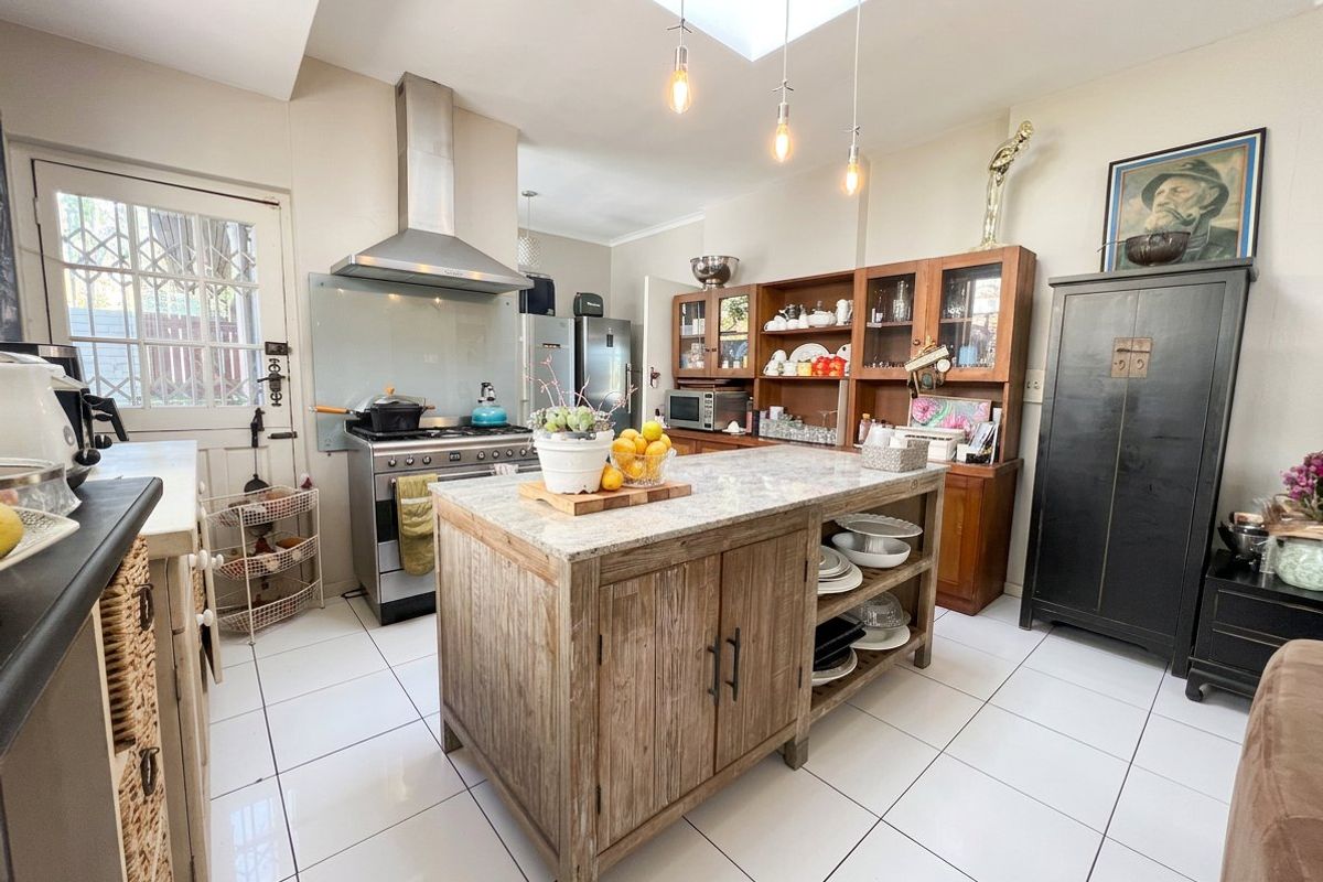 A well-lit kitchen featuring a central stone-topped island, stainless steel stove with extractor fan, and ample built-in cabinetry under a bright skylight.