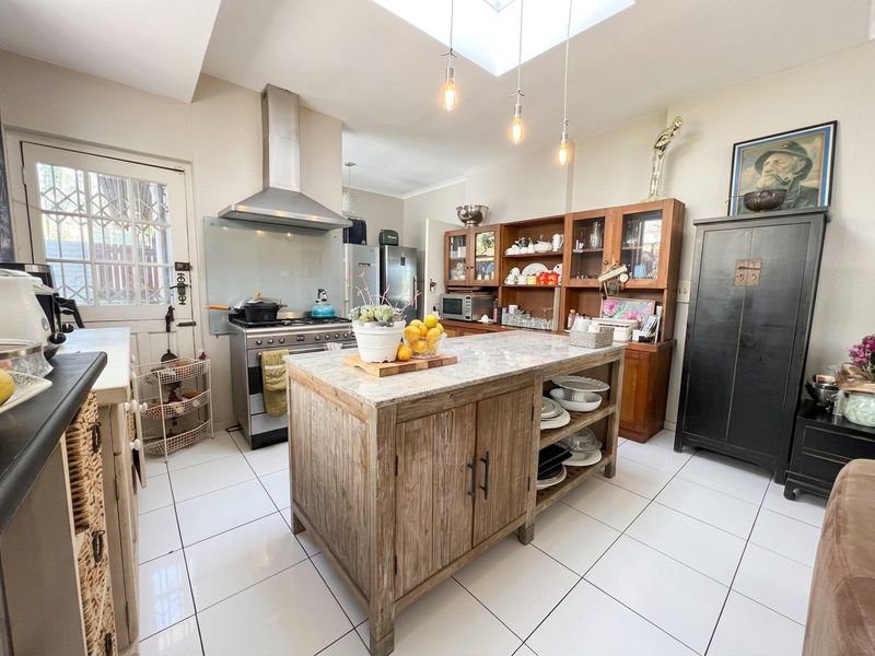 A well-lit kitchen featuring a central stone-topped island, stainless steel stove with extractor fan, and ample built-in cabinetry under a bright skylight.