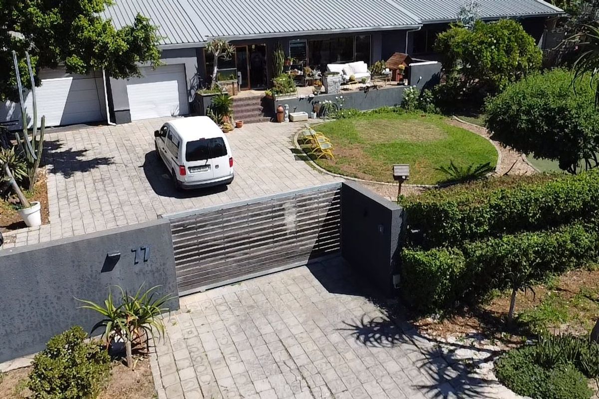 Aerial view of a residential property featuring a paved driveway, sliding gate, double garage, and a raised patio area.