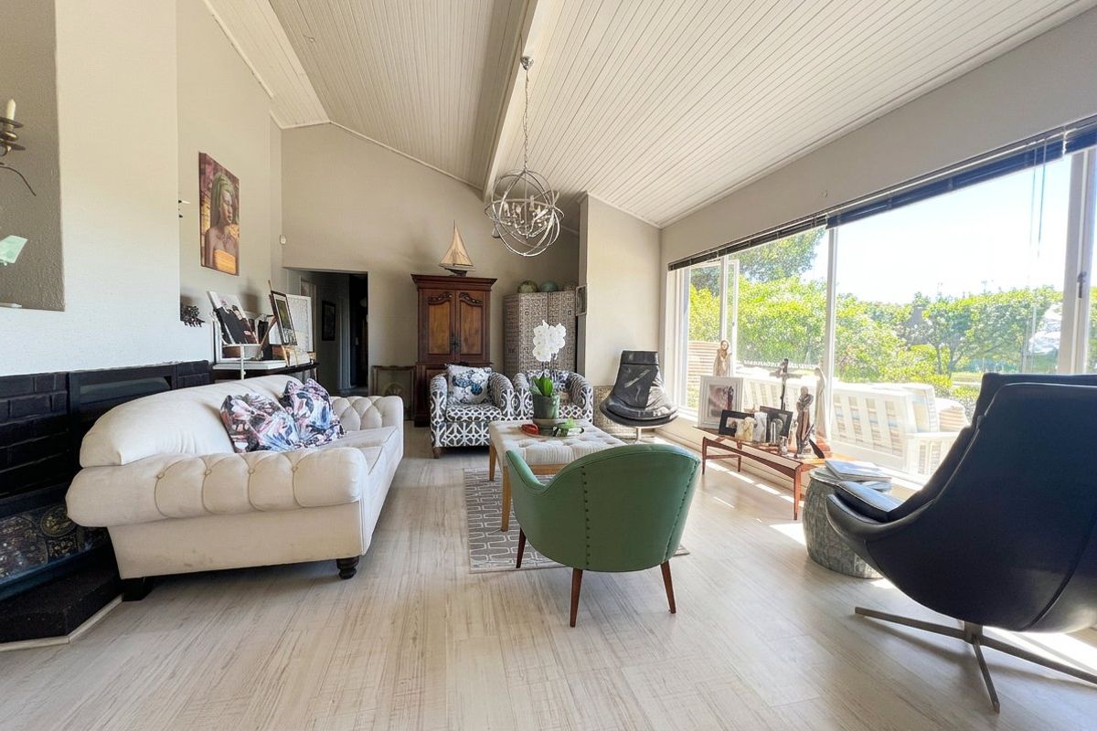 Spacious living room featuring a vaulted tongue and groove ceiling, fireplace, and large windows providing ample natural light and garden views.