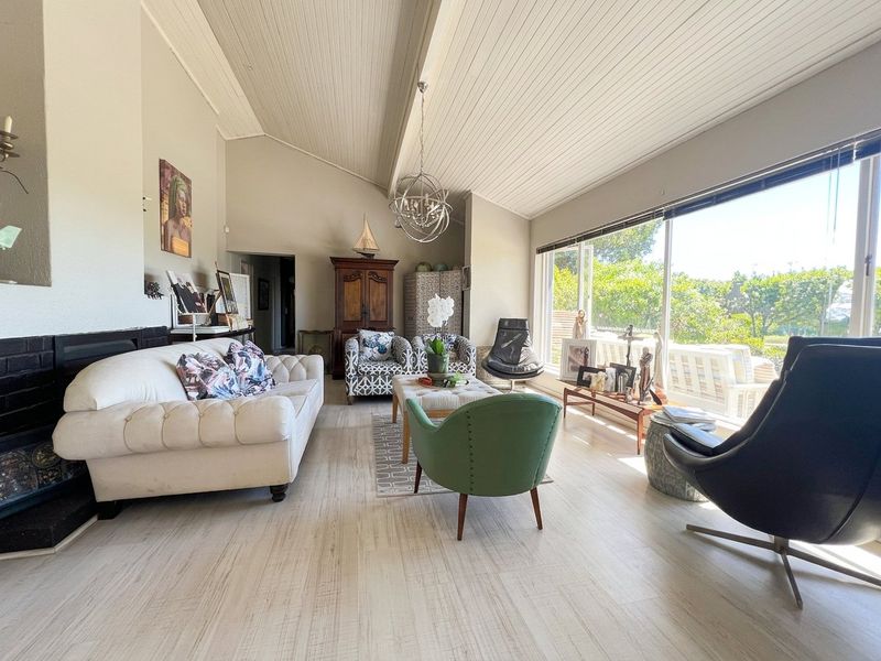 Spacious living room featuring a vaulted tongue and groove ceiling, fireplace, and large windows providing ample natural light and garden views.