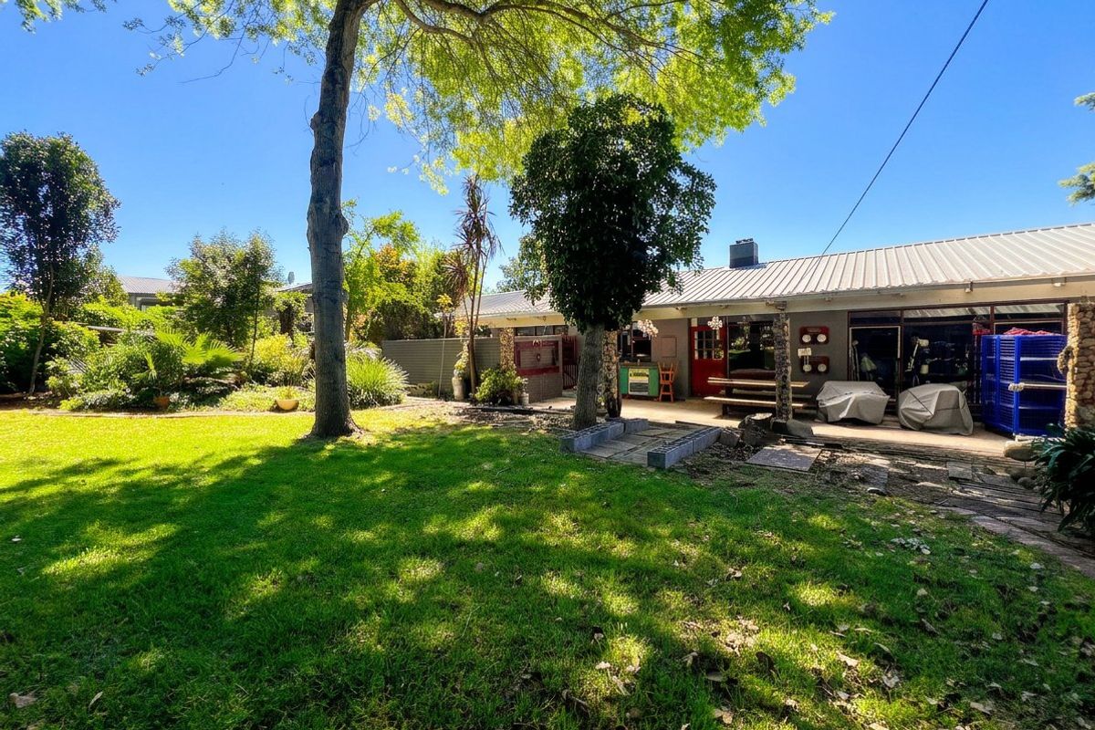 Spacious rear garden featuring a paved patio area, mature trees, and a home exterior with metal roofing and stone accents.