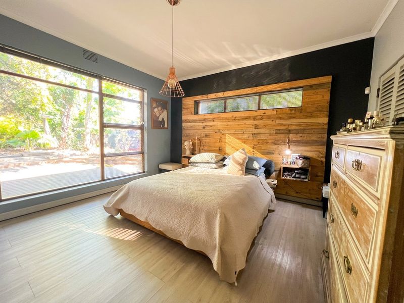 A well-lit bedroom featuring a timber accent wall, large windows providing natural light, and modern laminate flooring.