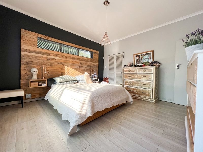 A well-maintained bedroom featuring light laminate flooring, a timber accent wall with a clerestory window, and louvered closet doors.