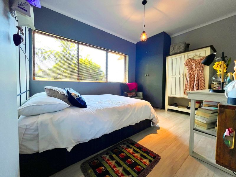 A well-lit bedroom featuring laminate flooring, a built-in wardrobe, and large windows with venetian blinds, creating a comfortable and functional living space.