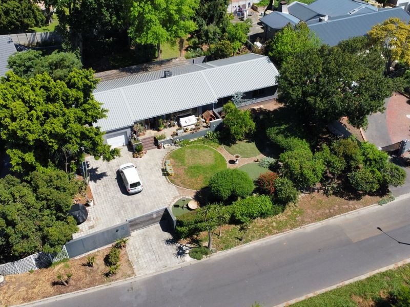 Aerial view of a residential property featuring a metal roof, paved driveway, and established landscaped garden.
