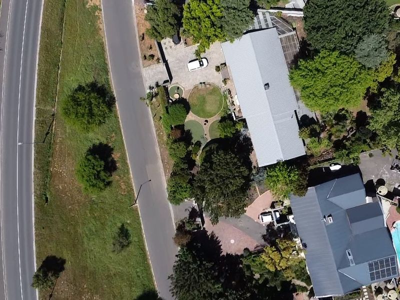 Aerial view of the property showing the main dwelling, swimming pool, solar panels, landscaped gardens, and paved driveway access from the street.