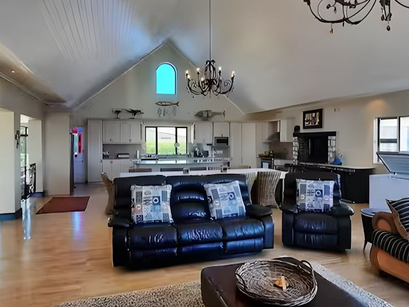 Spacious open-plan living and kitchen area featuring a high vaulted ceiling, exposed beams, and a large central kitchen island with integrated appliances.