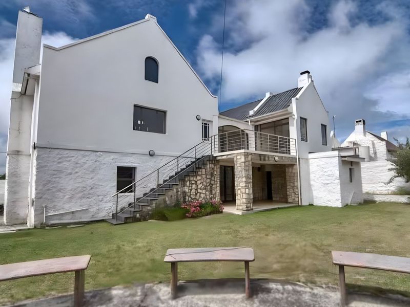 Rear view of a multi-level home featuring white rendered walls, stone accents, a metal staircase leading to a balcony, and a covered patio area.