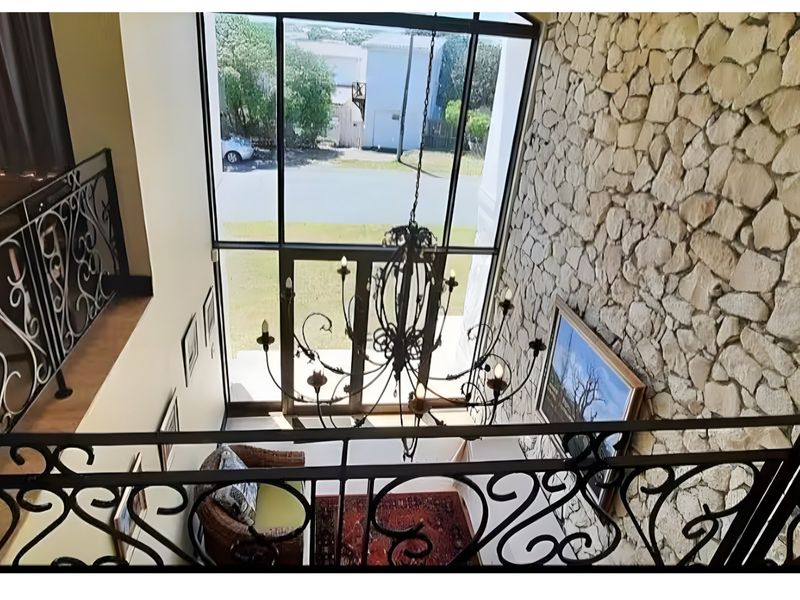 Double volume entrance hall featuring a striking stone feature wall, wrought iron balustrades, and a large chandelier overlooking the front garden.