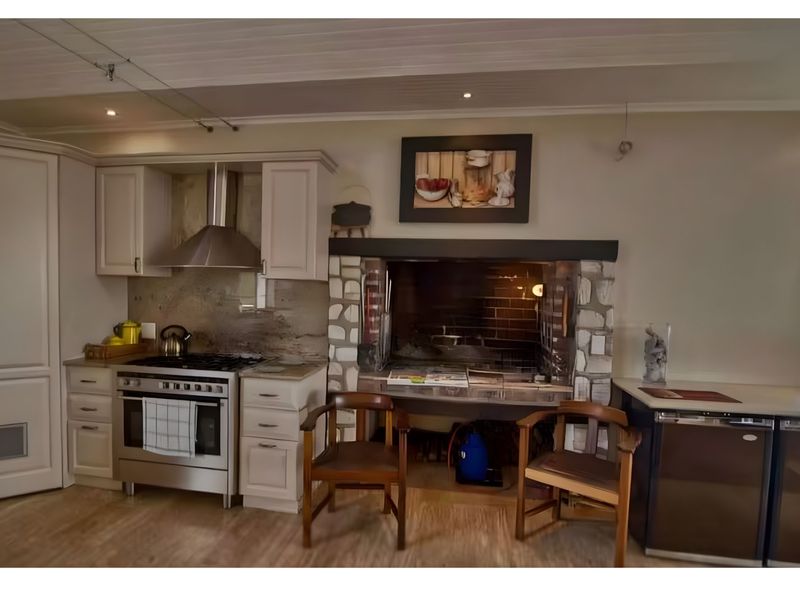Kitchen featuring built-in cabinetry, a stainless steel gas stove with extractor, and a prominent stone-clad indoor braai fireplace.