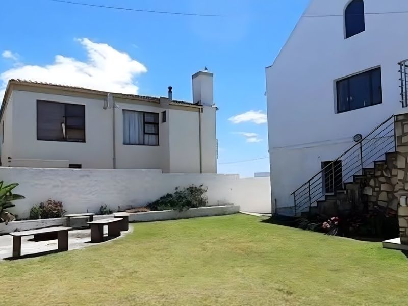 A well-maintained rear garden area featuring a lawn, stone-clad exterior wall, and an external metal staircase leading to the upper level.