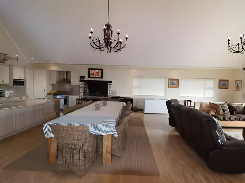 Spacious open-plan living area featuring a modern kitchen with island, dining space, and a stone fireplace under a high vaulted ceiling.
