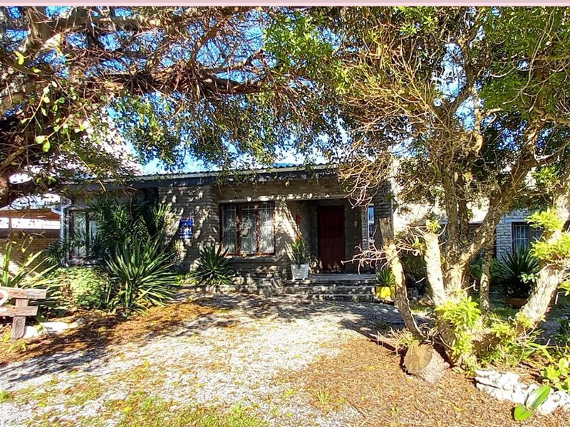 Front elevation of a stone-clad house featuring a gravel driveway and mature garden surroundings.