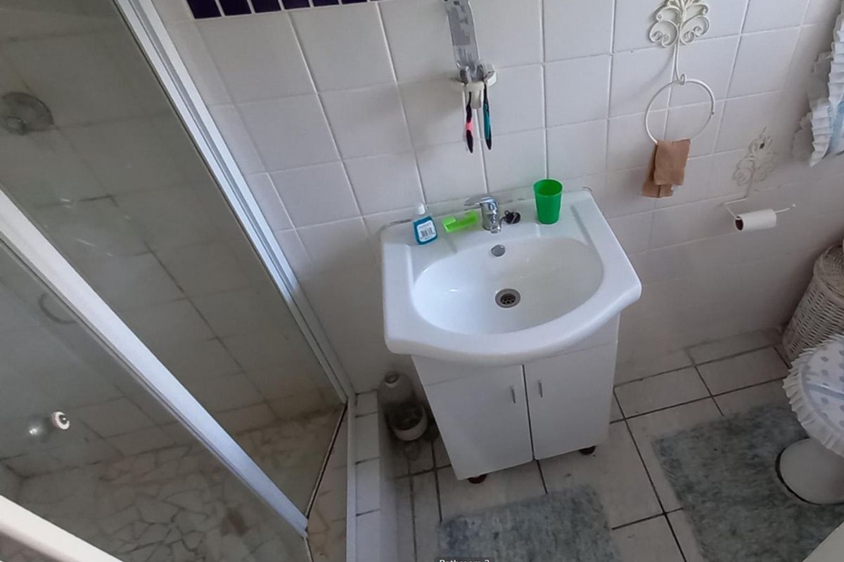 A functional bathroom featuring a vanity basin, shower enclosure, and tiled finishes, offering a practical layout with potential for modern updates.
