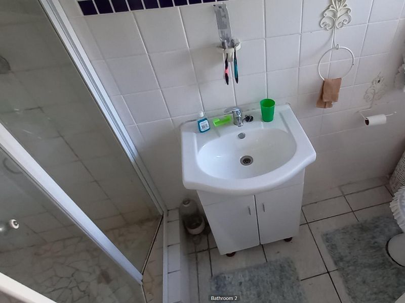 A functional bathroom featuring a vanity basin, shower enclosure, and tiled finishes, offering a practical layout with potential for modern updates.