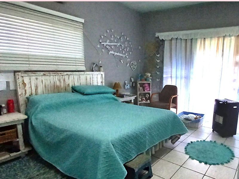 A bedroom featuring tiled flooring, a sliding glass door providing natural light, and venetian blinds.