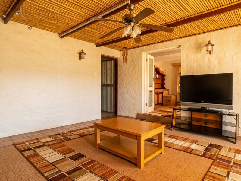 A living room featuring a textured bamboo ceiling, ceiling fan, and tiled flooring, providing a rustic aesthetic with direct access to adjacent rooms.