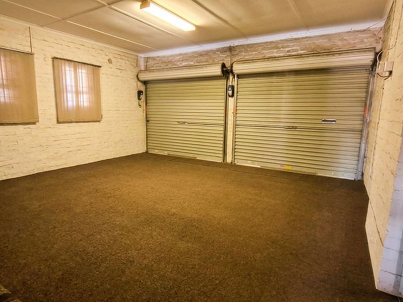 A spacious double garage featuring dual roller doors, painted brick walls, and carpeted flooring, providing secure parking or additional storage space.