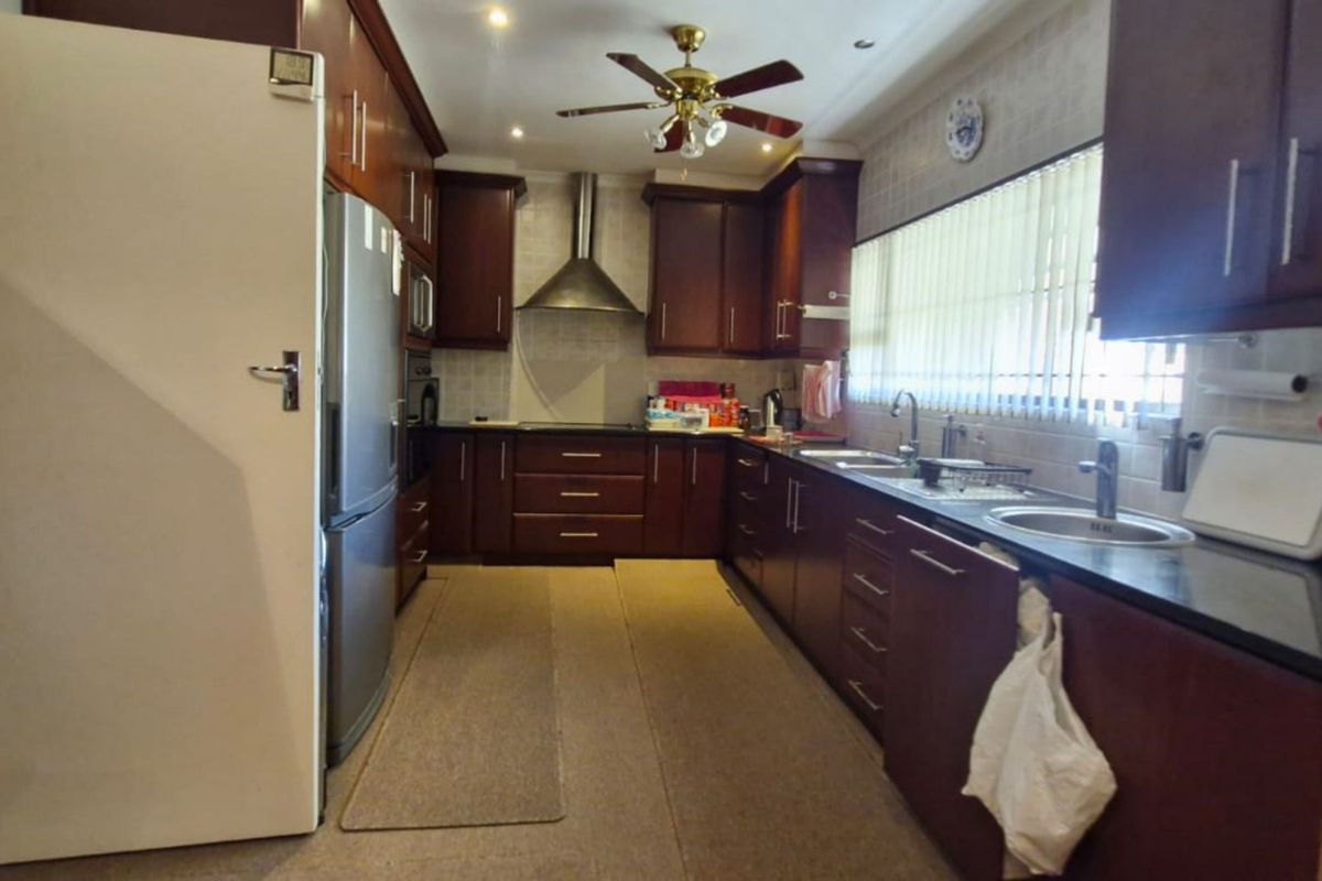 A functional kitchen featuring dark wood cabinetry, a stainless steel extractor fan, double sink, and tiled backsplash with recessed lighting.