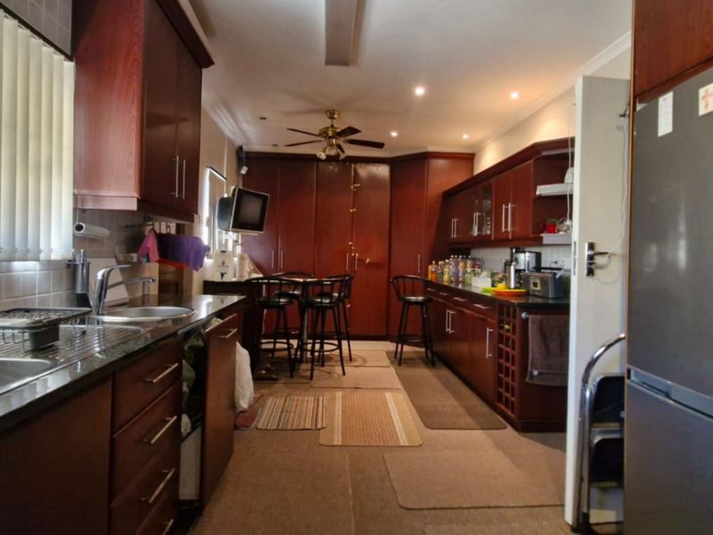 A functional kitchen featuring extensive dark wood cabinetry, granite countertops, double stainless steel sinks, and recessed lighting, offering ample storage and workspace.