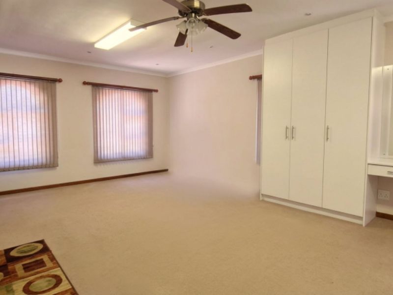 Spacious bedroom featuring neutral carpeting, ample built-in cupboard storage, a dedicated vanity area, and vertical blinds for privacy.