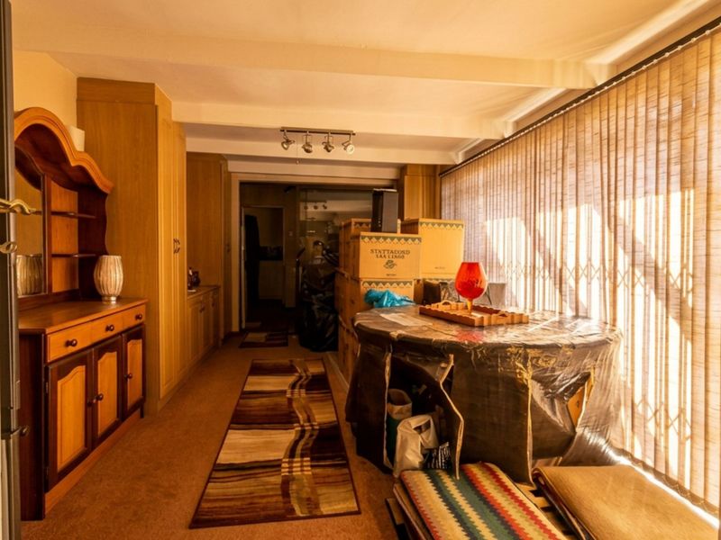 A living area featuring built-in wooden cabinetry, vertical blinds, and track lighting, currently used for storage.