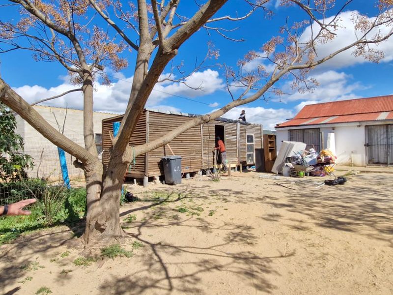Rear exterior view of the property showing a timber-clad structure and a main building with a corrugated metal roof.