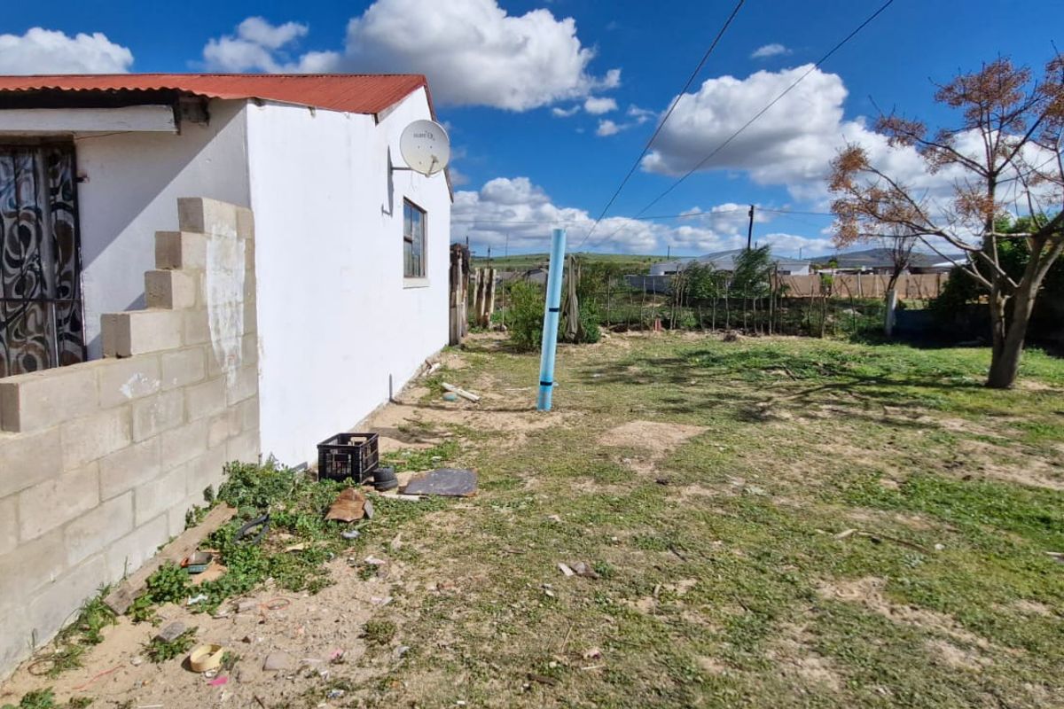 Rear exterior view of the property featuring a corrugated roof, security gate, and an expansive, undeveloped garden area with perimeter fencing.