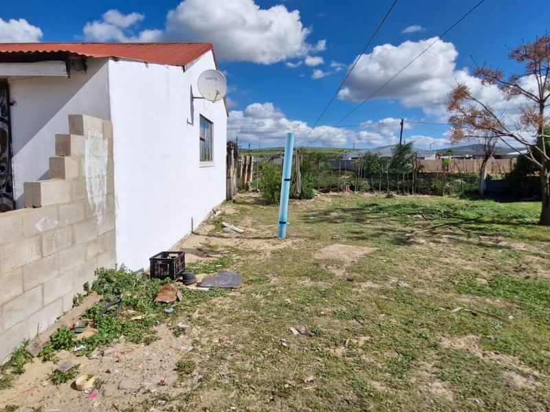 Rear exterior view of the property featuring a corrugated roof, security gate, and an expansive, undeveloped garden area with perimeter fencing.