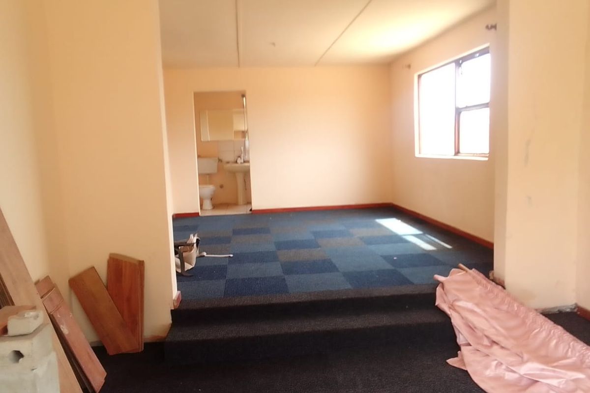 An empty bedroom featuring a raised platform area, blue carpeted flooring, and an attached en-suite bathroom.